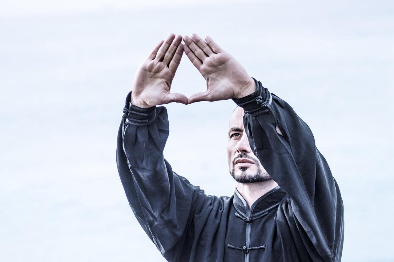 John Sammut in kimono, hands raised in symbolic gesture of consciousness